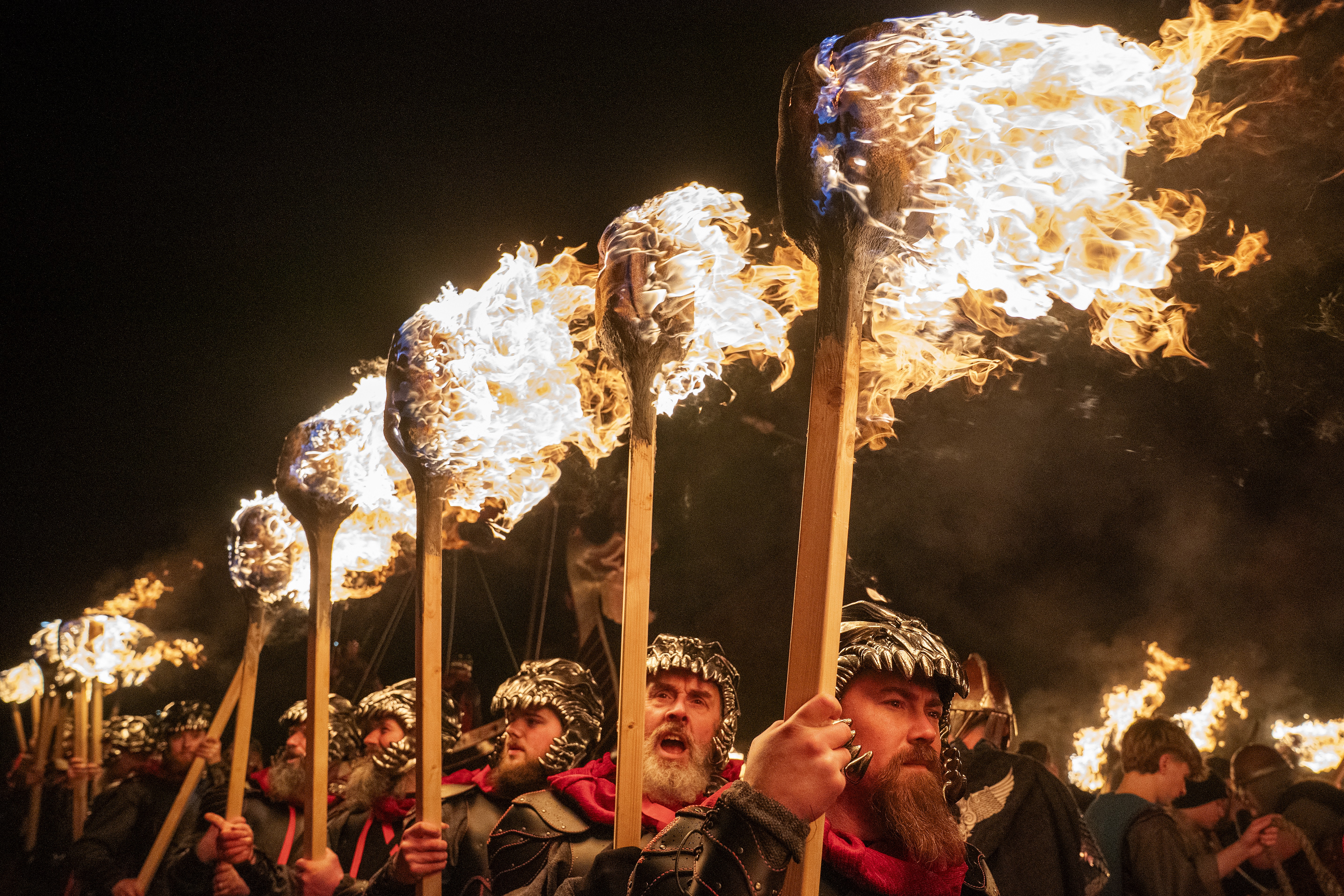 People dressed as Vikings hold large flaming torches during a parade.