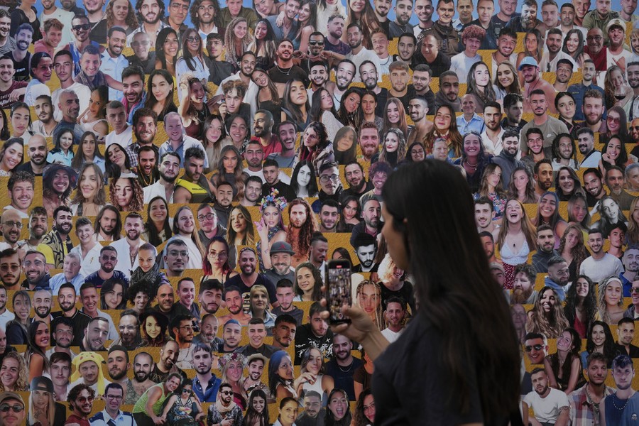 A person walks past a board covered with many photographs of young people.
