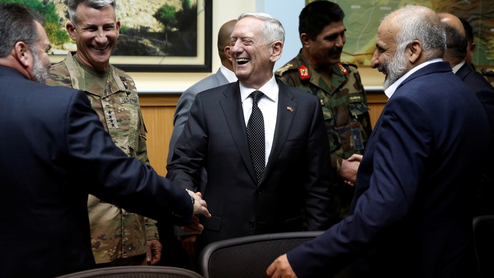 James Mattis stands in the center laughing and shaking hands with men in suits and military uniforms.