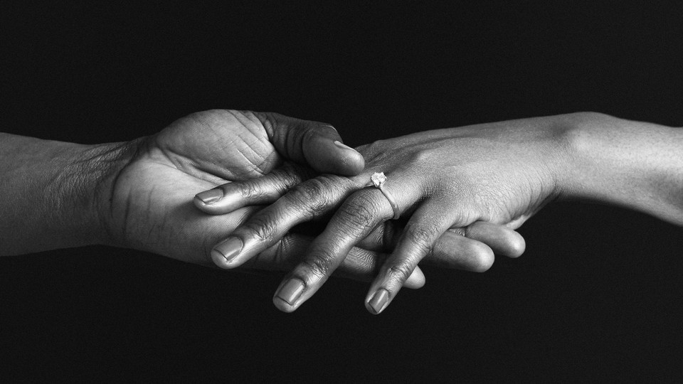 A photograph of one hand holding another hand that's wearing an engagement ring