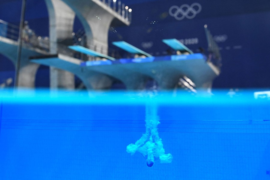 A diver is seen entering a pool, the camera lens at the surface, showing both an above and below view of the pool.