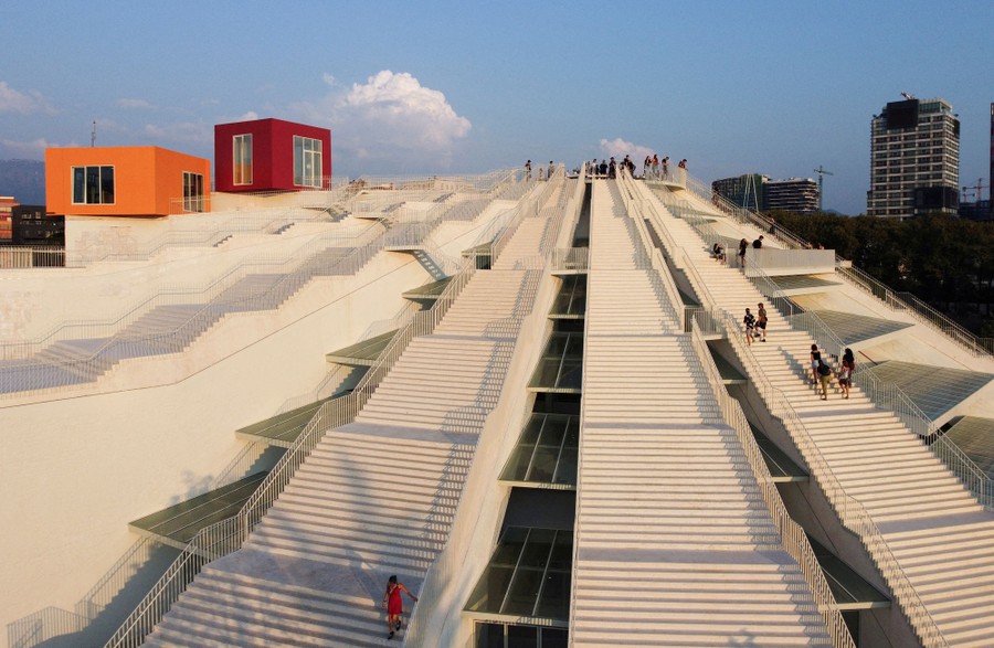 People walk on a few of many long staircases arranged in the shape of a pyramid.
