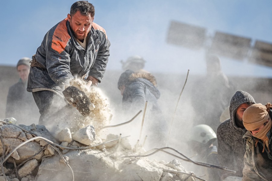 A half-dozen people are seen removing debris from the top of a collapsed building.