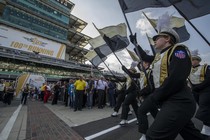 Students in black and gold marching-band uniforms hold Purdue flags and walk in tandem. 