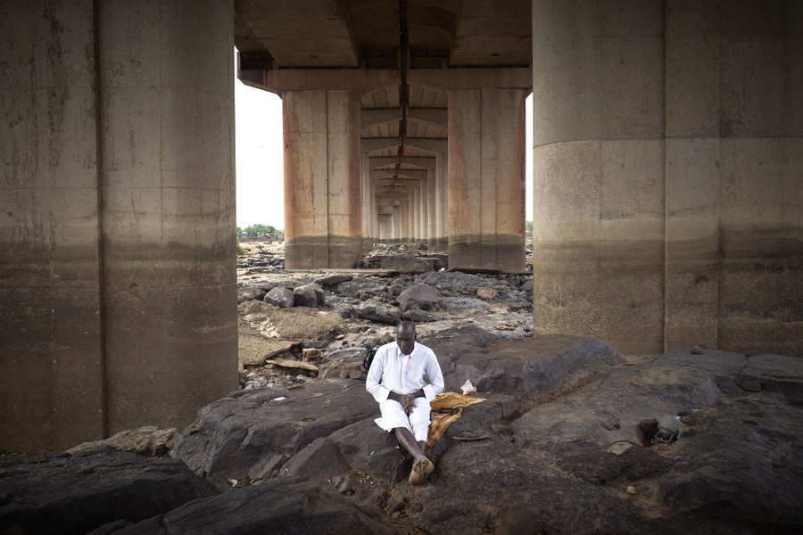 A man sits alone beneath a long road bridge.
