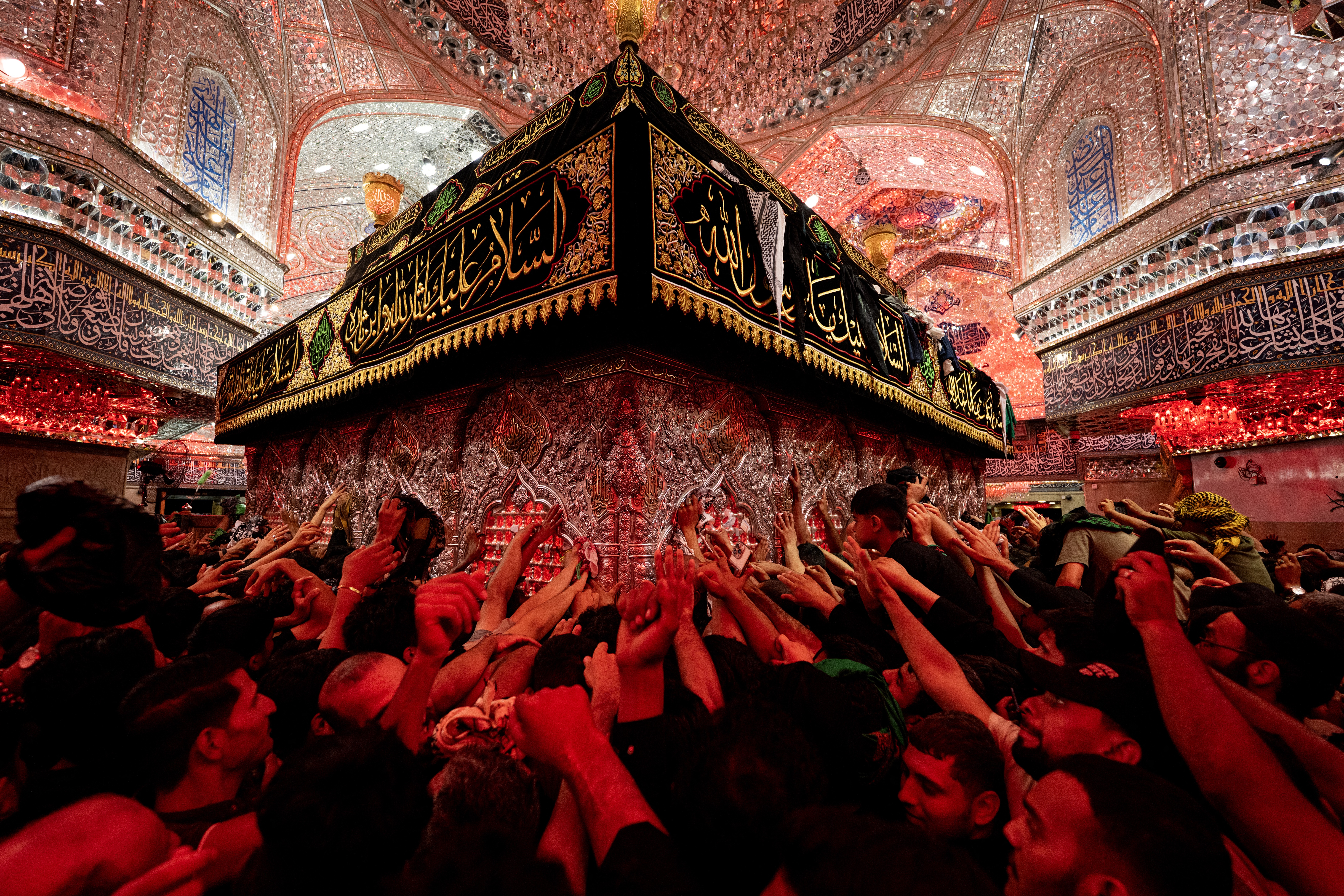 Many worshipers in a shrine reach out to touch a tomb.