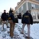 Photograph of several FBI agents standing in the snowy front yard of a green and white house.