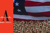 This photo shows a wide shot of U.S. army members saluting and wearing fatigues and matching red berets. Behind them is the image of the American flag