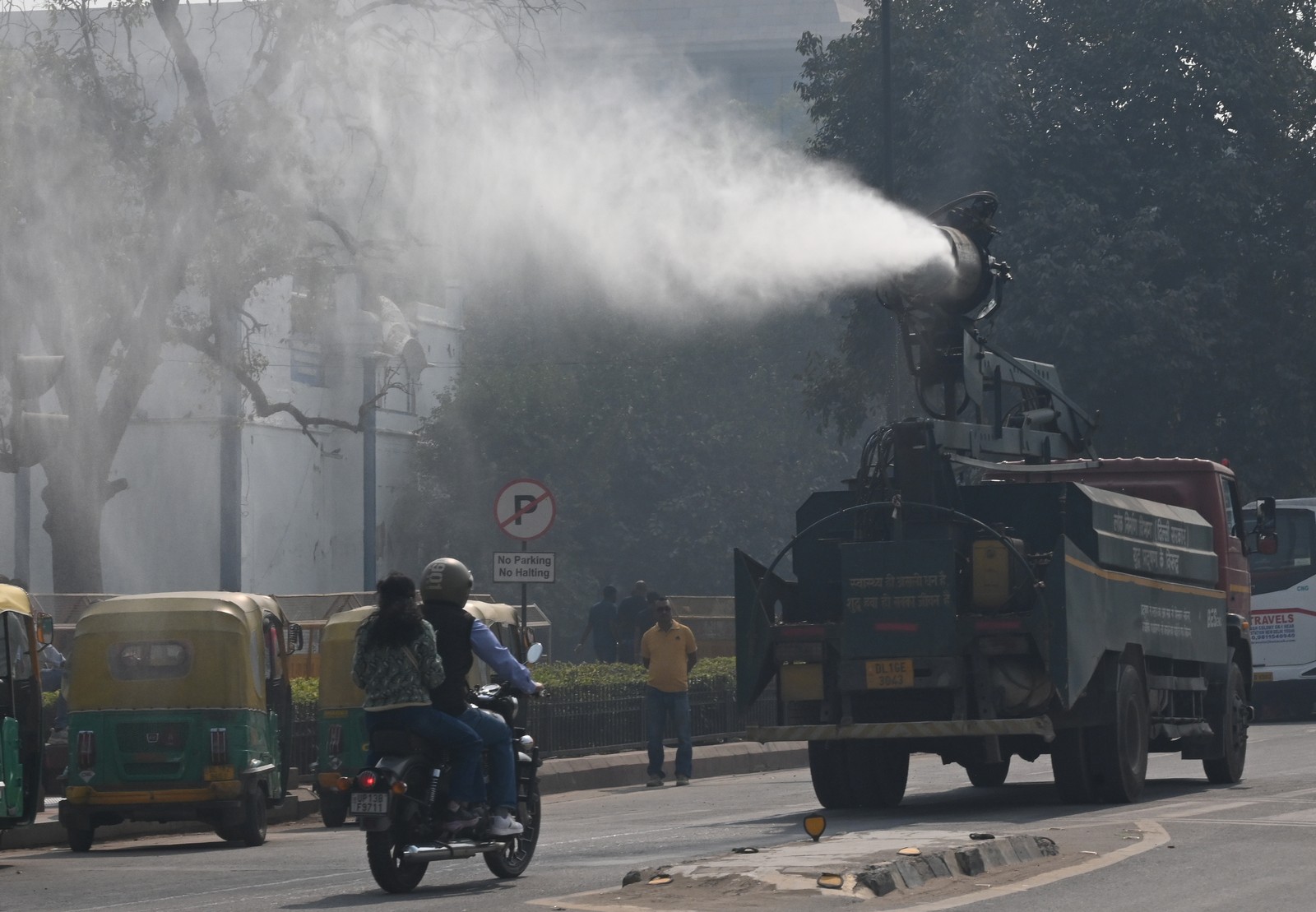 A device mounted to the top of a truck sprays a mist of water in the air as it drives down a road.