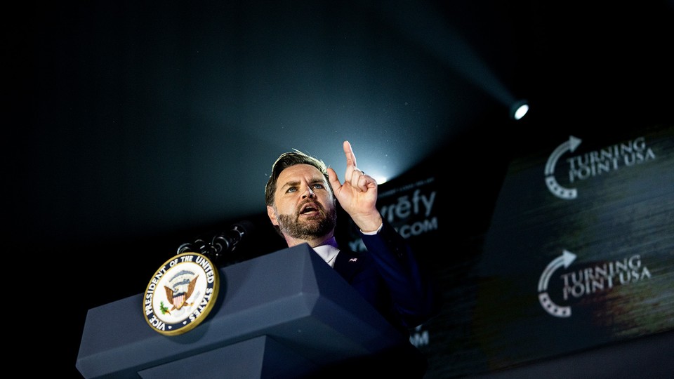 A view from below as Vance speaks with a finger raised in front of a backdrop that reads "Turning Point USA"