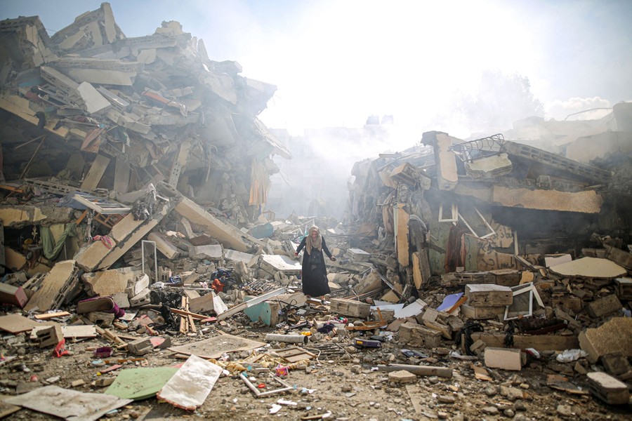A person walks through debris, surrounded by huge piles of rubble from war-destroyed buildings.