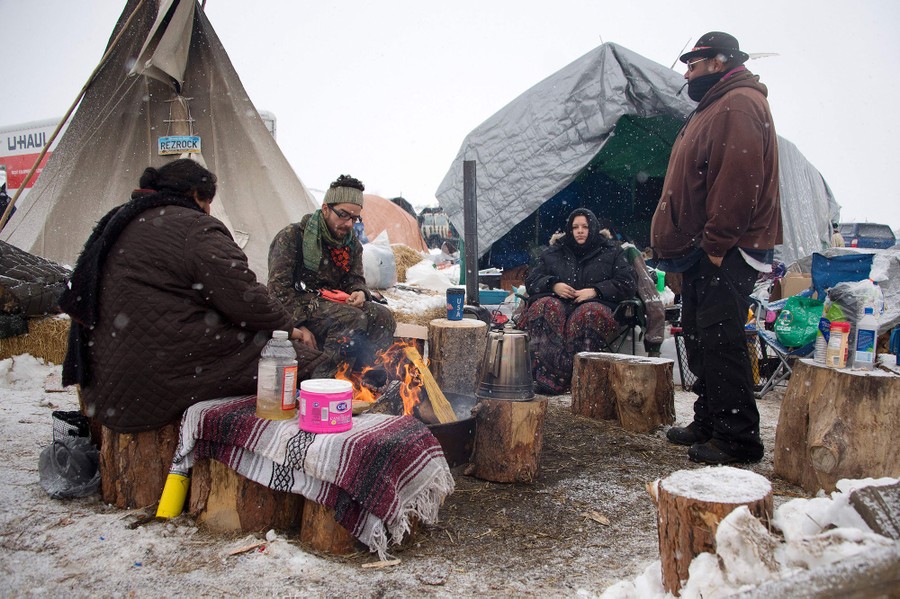 Activists sit around a camp fire as it snows at the Oceti Sakowin camp on December 5, 2016.