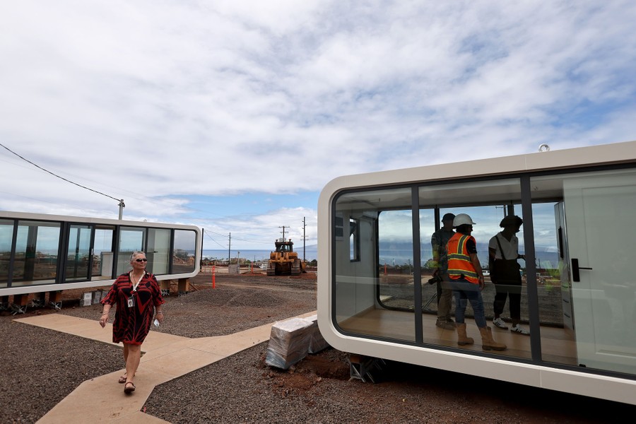 Several people walk in and around a couple of small modern temporary residential units.