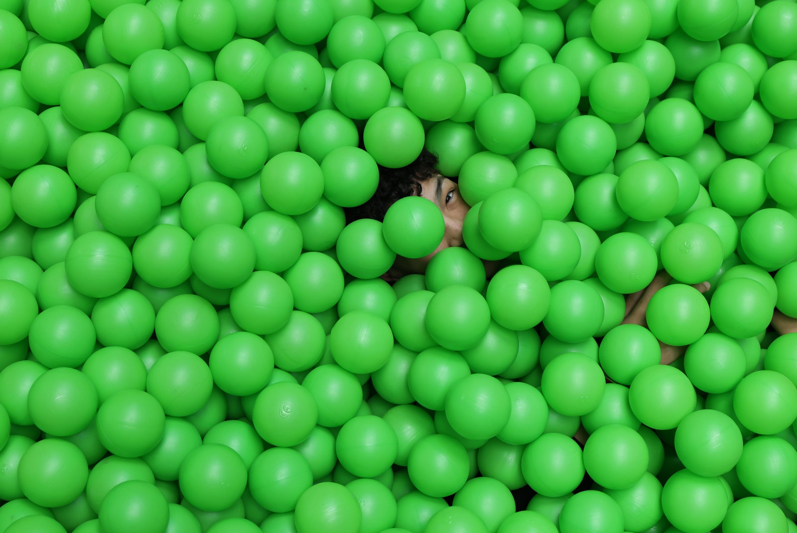 A person lies in a bin of green plastic balls