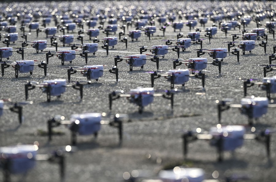 Many rows of small drones sit on the ground before a drone show.