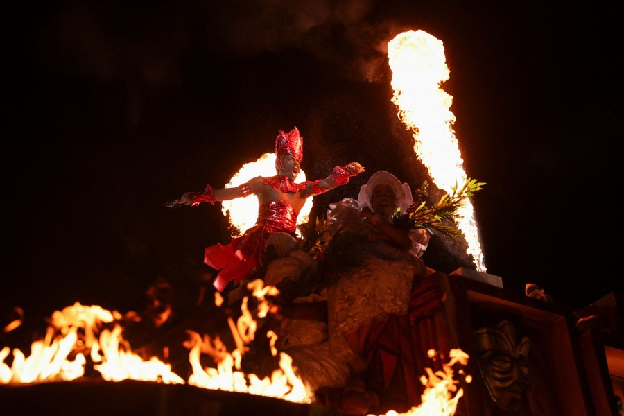 Costumed performers dance, backdropped by pyrotechnic displays.