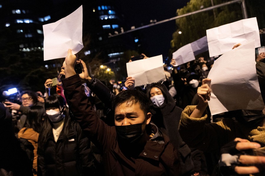 Protesters gather, with some holding up blank sheets of paper.