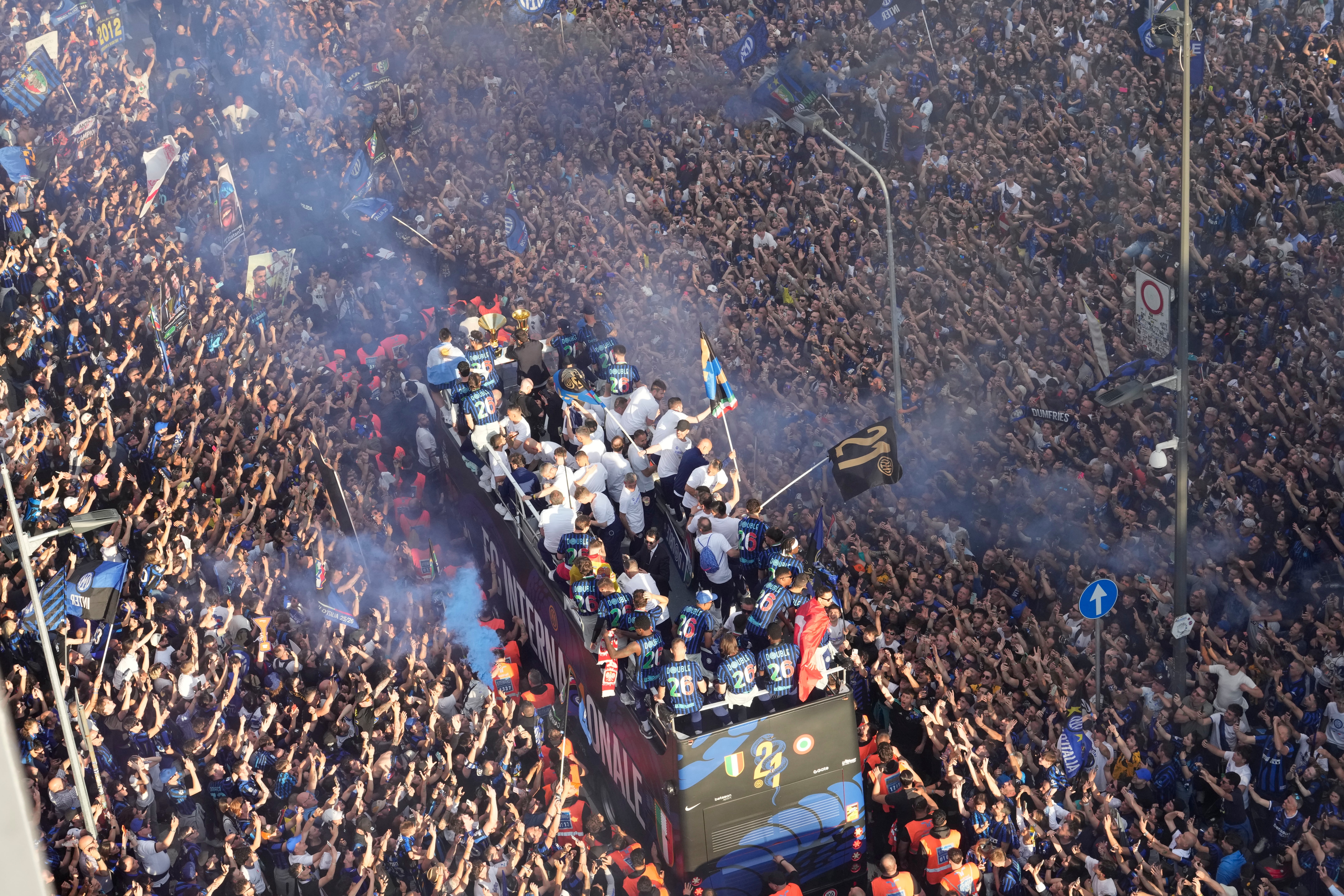 Thousands of fans cheer along a street as a bus carries a champion soccer team past a stadium.