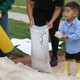 A child holds a scoop to help fill sandbags.
