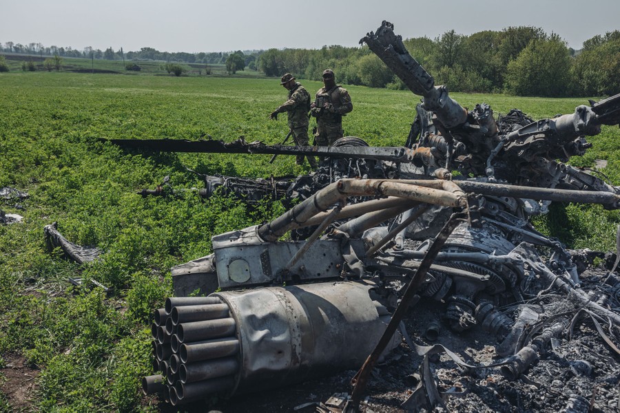 Two soldiers walk near a downed Russian helicopter in a field.