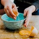 A picture of someone cracking an egg on a bowl but spilling the yolk onto a table