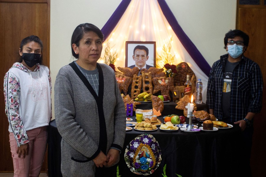 A family stands near a table of food offerings, and a portrait of a deceased family member.