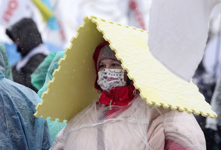 A person stands among others in the rain, wearing protective plastic.