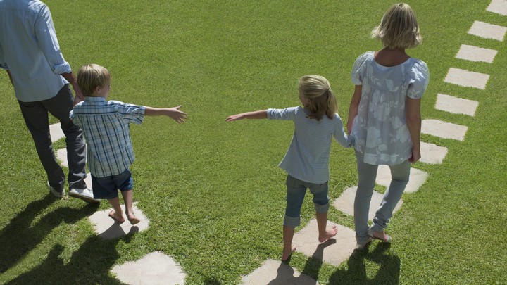 A man and woman lead two small children away from each other by the hand.
