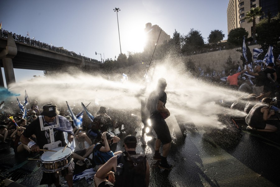 A crowd of protesters in a street is hit with a water cannon.
