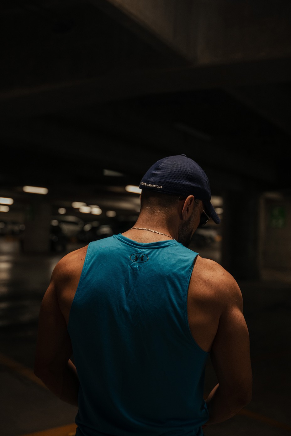 a muscular man in a light blue tank top and a baseball cap facing away
