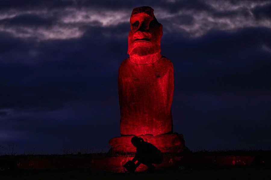 A person places a red light at the foot of an ancient stone statue.