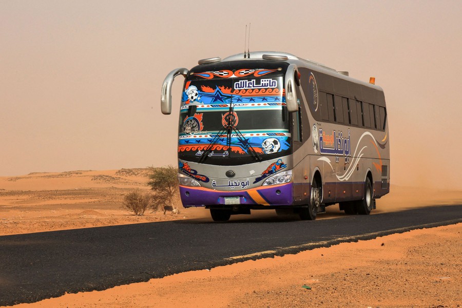 A passenger bus drives down a desert road.
