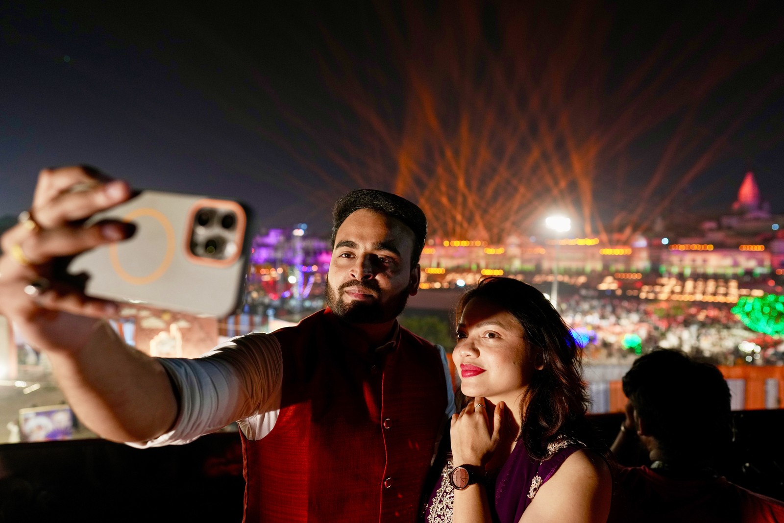 A couple takes a selfie in front of a bright light show.