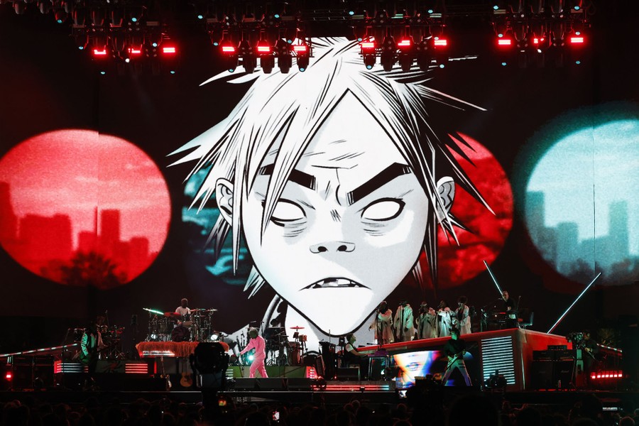 A large video screen featuring a cartoon character stands behind a group of musicians performing on stage.