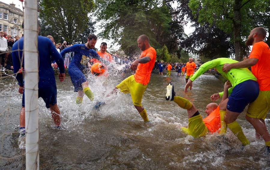 People splash while playing a game of soccer in an ankle-deep stretch of a river.