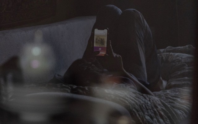 A teenager lying on a couch, looking at a cell phone.