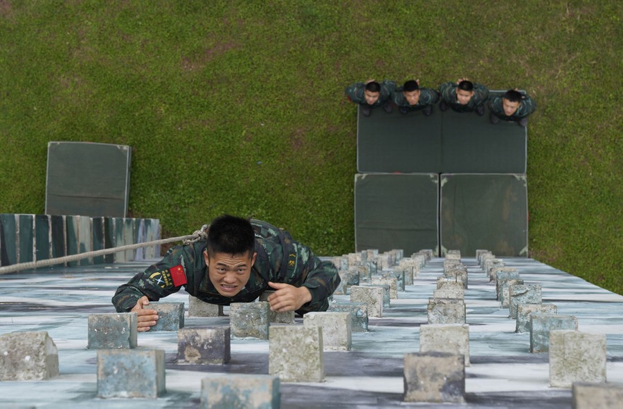 A Chinese soldier climbs a high wall as four others watch below.