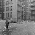 A black-and-white photo of a child running through New York City tenements