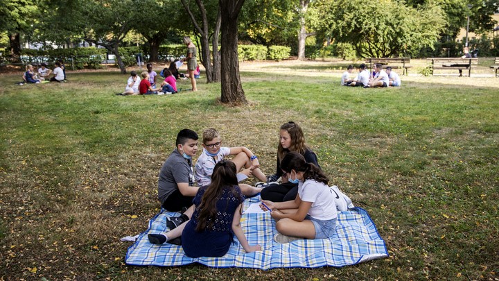 Groups of kids sit spread out on blankets in a park.