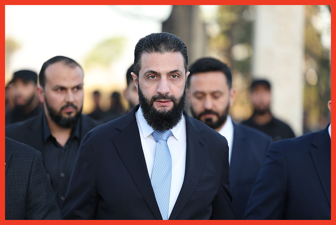 color photo of bearded man wearing suit jacket and dress shirt with light-blue tie