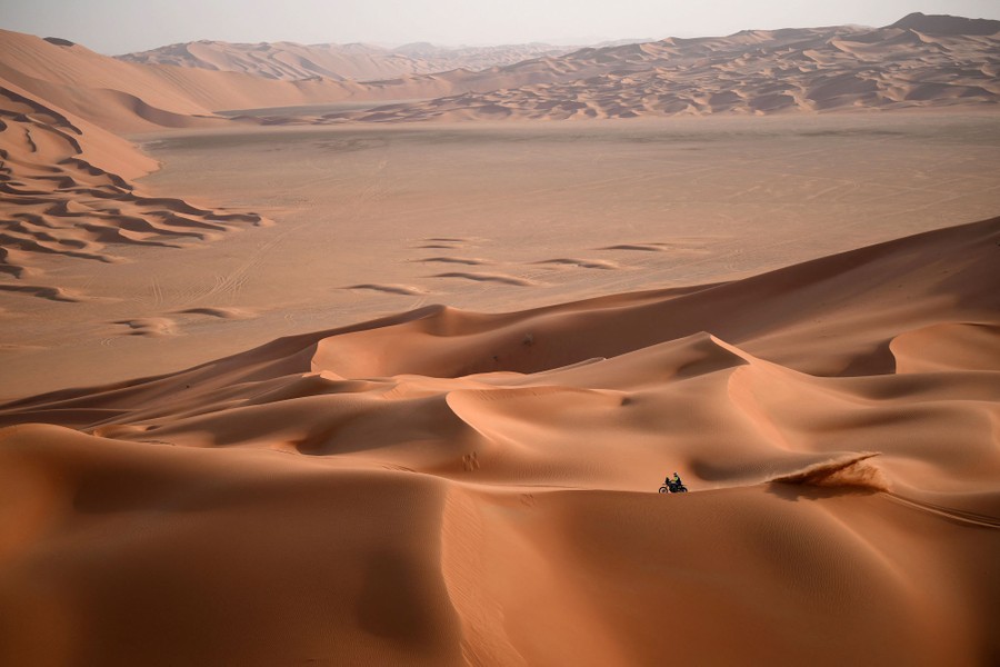 A motorcyclist rides across sand dunes.