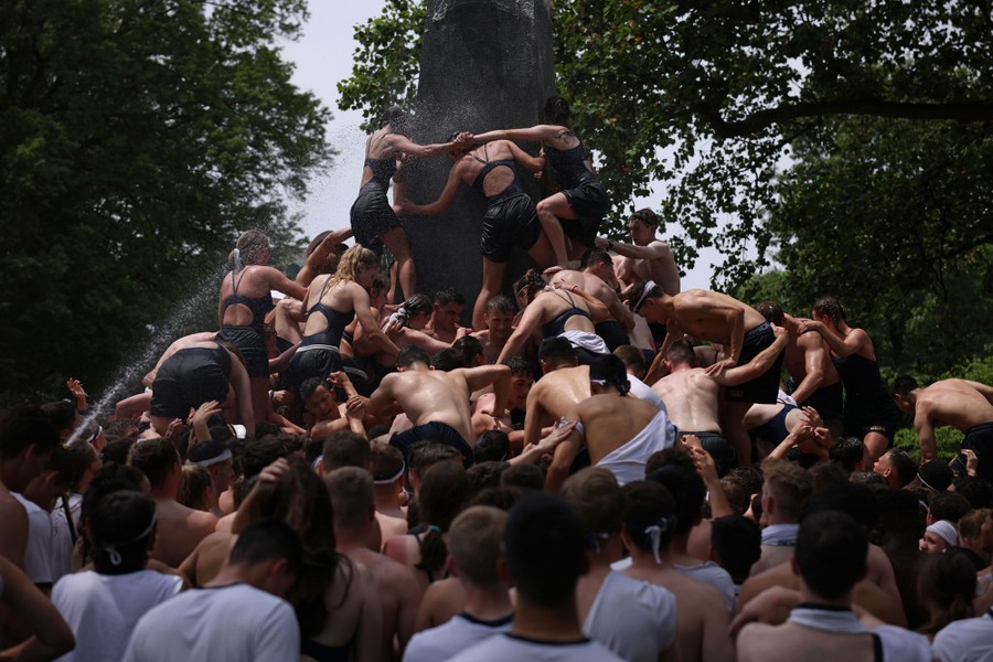 Dozens of midshipmen clamber over one another to scale a tall obelisk.