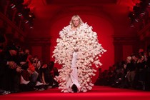 A model wearing a long coat made of stuffed animals walks down a runway.
