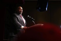 A color photograph of Mark Robinson, in a suit, speaking from a lectern