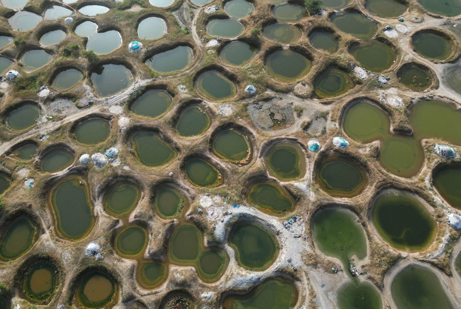 An elevated view of many close-set rounded pools of water—salt wells—in a field