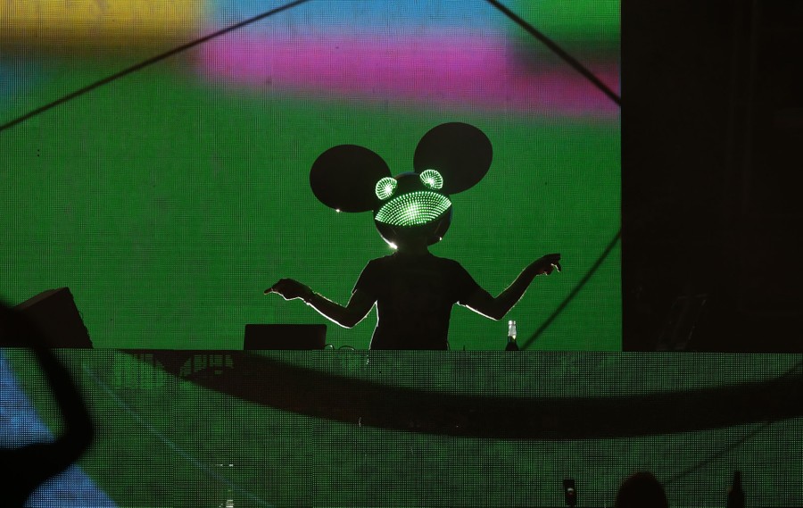 A person wearing a large illuminated mouse helmet plays dance music.