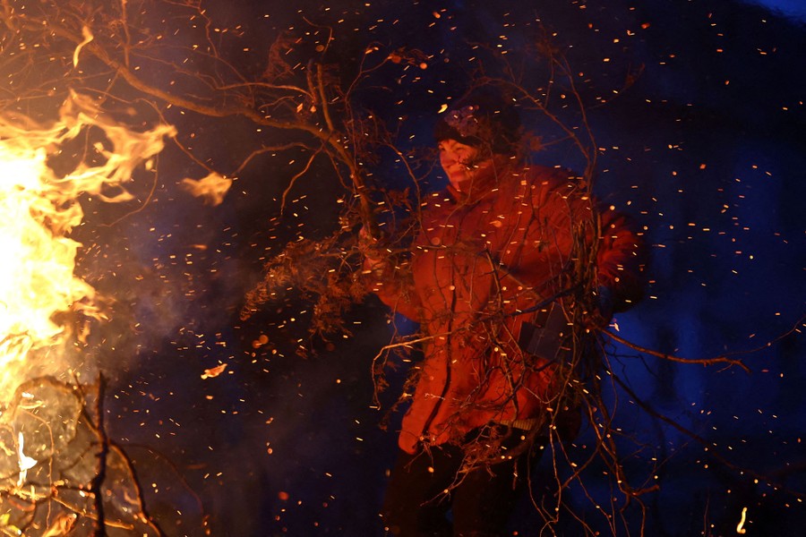A person carries branches toward a sparking fire.