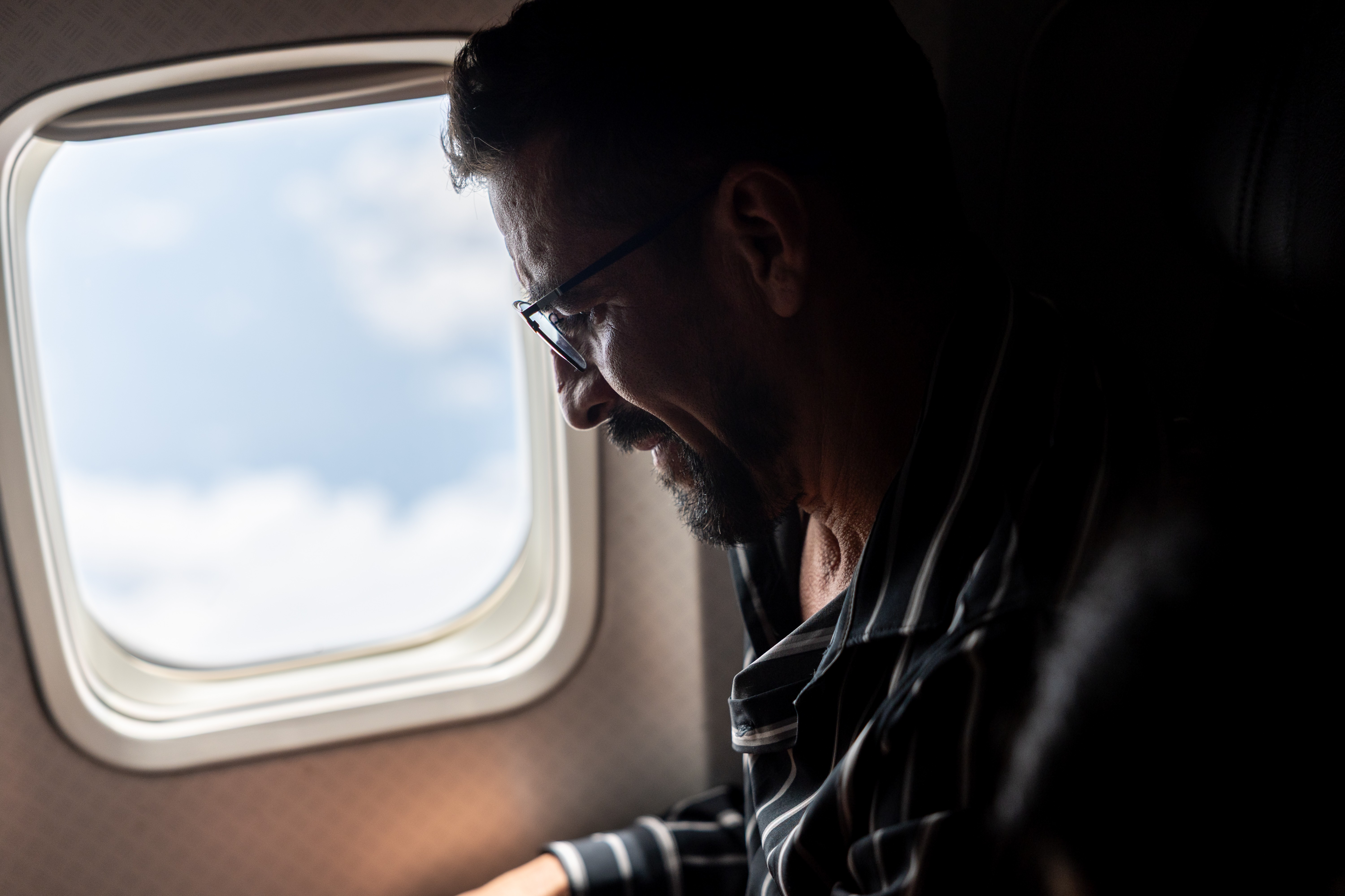 A man, seated in a window seat on an airplane