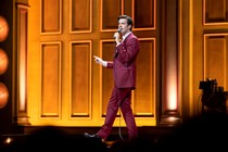The comedian John Mulaney onstage with a microphone in his hand