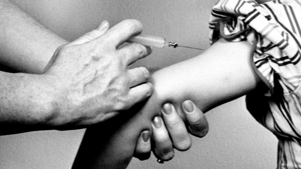 A person holds a syringe next to a child's arm